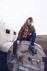 Девушка в теплой одежде сидит на сломанном самолете между темными землями в Исландии — стоковое фото