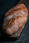 Pão rústico caseiro em tábua de madeira sobre fundo escuro — Fotografia de Stock
