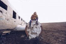 Young lady in warm wear sitting on broken aircraft between dark grounds in Iceland — Stock Photo