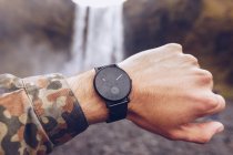 Mão de corte de cara mostrando relógios pretos perto de cascata de água na Islândia em fundo borrado — Fotografia de Stock