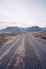 Strada di campagna tra terre selvagge che conducono alle montagne e bel cielo in Islanda — Foto stock