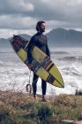 Молодой человек в гидрокостюме с доской для серфинга ходит по морскому побережью — стоковое фото