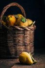 Плоды айвы на темном деревянном фоне с корзиной на заднем плане — стоковое фото