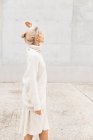 Вид збоку красивої молодої леді в елегантному теплому вбранні, що тримає очі закритими під час ходьби на тротуарі біля білої стіни — стокове фото