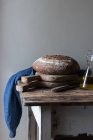 Fresh wholegrain bread loaf on rustic wooden table with bottle of oil — Stock Photo