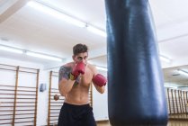 Young bearded guy training in gym with punch bag — Stock Photo