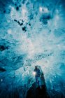 Путешественник с горящим факелом, стоящим в зале кристально голубой ледяной пещеры, Исландия — стоковое фото