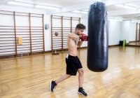 Junger Bärtiger trainiert mit Boxsack in Turnhalle — Stockfoto
