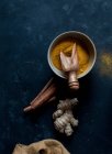 Bowl with dried turmeric and root of fresh ginger and cinnamon on dark background — Stock Photo