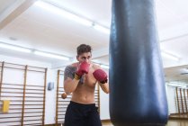 Giovane barbuto ragazzo formazione in palestra con sacco da boxe — Foto stock