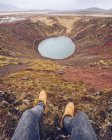 De arriba recortar las piernas humanas cerca del lago en el cráter entre las tierras marrones de la muerte y colinas en Islandia - foto de stock