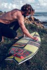 Молодий чоловік прибирає дошку для серфінгу на узбережжі океану — стокове фото