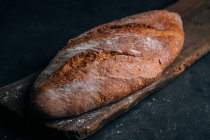 Hausgemachter rustikaler Brotlaib auf Holzbrett auf dunklem Hintergrund — Stockfoto