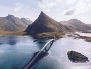 Vue pittoresque sur les drones des montagnes et de la chaussée avec un pont qui coule parmi les eaux bleues de l'océan des îles Lofoten — Photo de stock