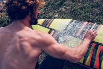 Primer plano de hombre joven limpieza tabla de surf de colores en la hierba - foto de stock