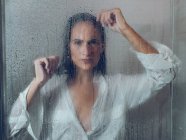Sopping mujer en camisa de pie en cabina de ducha y mirando a la cámara - foto de stock