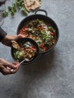 Mani umane che tengono ciotola sopra pentola di ragù con lenticchie e patate dolci al curry e ciotola su tavolo grigio — Foto stock