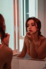 Reflet d'une femme brune passionnée et attrayante portant du rouge à lèvres devant le miroir — Photo de stock