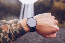 Crop hand of guy showing black watches near water cascade in Iceland on blurred background — Stock Photo