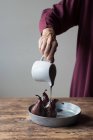 Неузнаваемая женщина наливает винный сироп из вкусного гороха, стоя у деревянного стола — стоковое фото