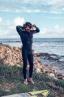 Молодий чоловік одягає гідрокостюм на морському узбережжі з дошкою для серфінгу — стокове фото