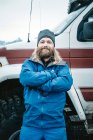 Homem barbudo adulto confiante em roupas que se apoiam no carro off road com os braços cruzados olhando para a câmera, Islândia — Fotografia de Stock