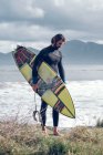 Giovane in muta con tavola da surf che cammina sulla costa del mare — Foto stock