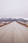 Strada di campagna tra terre selvagge nella neve che conduce a montagne e cielo tra le nuvole in Islanda — Foto stock