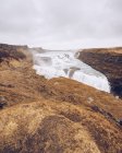 Grande cascata de água fluindo entre terras mortas e caindo entre rochas na Islândia — Fotografia de Stock