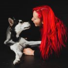 Jovem mulher com cabelo vermelho brilhante olhando para filhote de cachorro bonito Siberian Husky — Fotografia de Stock