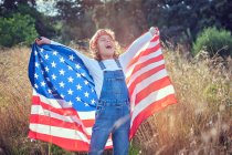Niño feliz con los ojos cerrados sosteniendo la bandera americana en el campo - foto de stock
