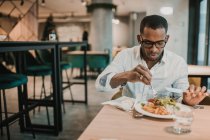 Adulto afro-americano masculino desfrutando de deliciosa comida enquanto sentado à mesa em restaurante elegante — Fotografia de Stock