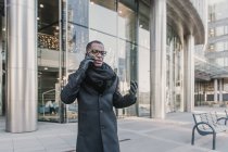 Schöner afrikanisch-amerikanischer Geschäftsmann in stylischer warmer Kleidung, der auf der Straße der modernen Stadt mit dem Smartphone spricht — Stockfoto