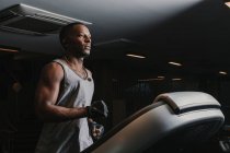Side view of handsome African American guy in sportswear listening to music and running on treadmill — Stock Photo