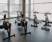 Varias máquinas de ejercicio modernas de pie cerca de una gran ventana en el interior increíble gimnasio elegante - foto de stock