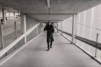 Homem afro-americano em roupa elegante andando na passagem do edifício moderno e tendo conversa smartphone — Fotografia de Stock