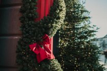 Fluffy conifer garlands with bows hanging on red pillars near walls of lovely building on sunny day — Stock Photo