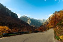 Pittoresca veduta della strada asfaltata vuota che attraversa una meravigliosa catena montuosa durante il soleggiato autunno diurno — Foto stock