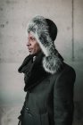 Side view of handsome African American man in stylish fur hat standing near concrete wall — Stock Photo