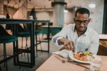 Hombre afroamericano adulto disfrutando de una deliciosa comida mientras está sentado en la mesa en un restaurante elegante - foto de stock
