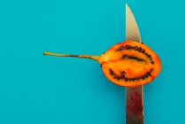 Острый нож нарезает вкусный спелый тамарилло на ярко-голубом фоне — стоковое фото