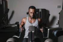 Hombre negro haciendo ejercicio en la máquina en el gimnasio - foto de stock