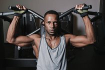 Sério afro-americano cara ouvir música e realizar exercício na máquina moderna durante o treino no ginásio — Fotografia de Stock