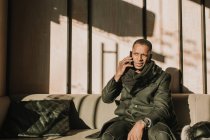 Bell'uomo afroamericano in abito caldo che tiene una tazza di bevanda calda e distoglie lo sguardo mentre si siede su un comodo divano nel caffè — Foto stock