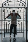 Visão traseira do cara afro-americano em sportswear usando equipamentos de ginástica enquanto trabalhava perto da janela — Fotografia de Stock