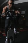 Серйозний чорний чоловік на тренувальному велосипеді в тренажерному залі — стокове фото