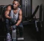 Attrayant Afro-Américain en vêtements de sport écouter de la musique dans les écouteurs et regarder loin dans la salle de gym moderne — Photo de stock