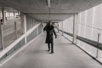 Uomo afroamericano in abito elegante camminare nel passaggio di edificio moderno e avere conversazione smartphone — Foto stock