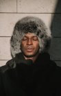 Hombre afroamericano guapo con los ojos cerrados en ropa de abrigo con estilo de pie cerca de la pared de hormigón - foto de stock