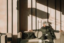 Bello uomo afroamericano in abito caldo guardando altrove mentre seduto su un comodo divano in caffè — Foto stock